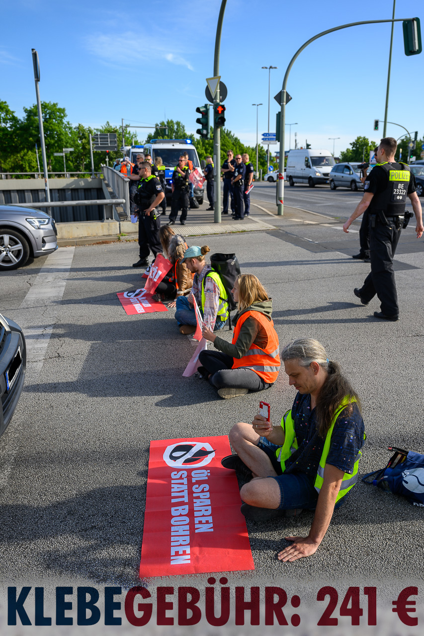 Menschen blockieren eine Straße. Auf einem Banner steht die Forderung „Öl sparen statt bohren“.