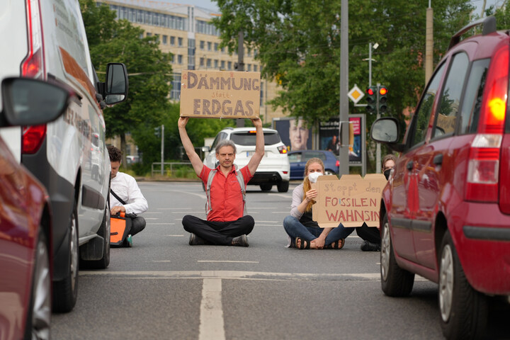 Menschen sitzen auf der Straße. Ich halte ein Schild hoch: Dämmung statt Erdgas.