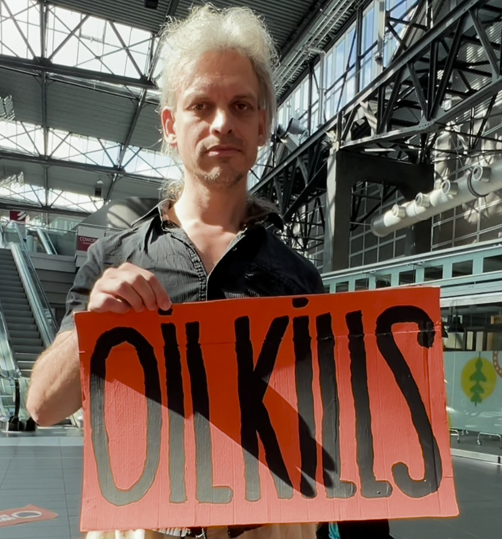 Christian Bläul hält ein Schild "Oil kills", übersetzt "Öl tötet". Gemeint ist Erdöl, die Grundlage von Kerosin.